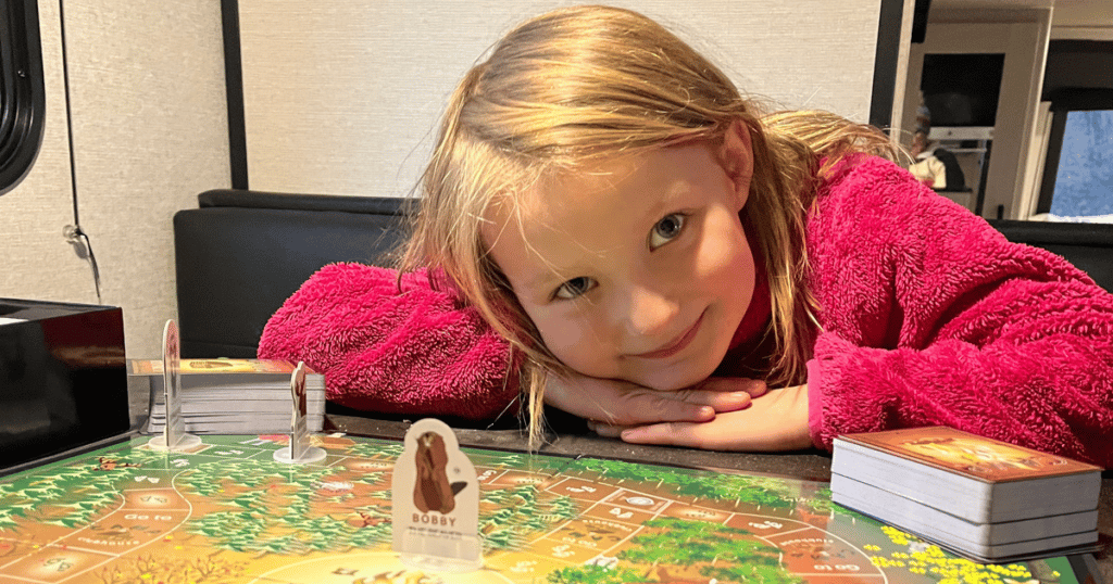 Josie smiling with the board game "Camp" in the camper