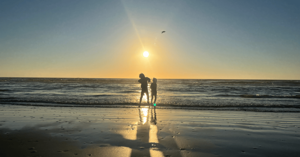A photograph of two kids jumping in the ocean at sunset