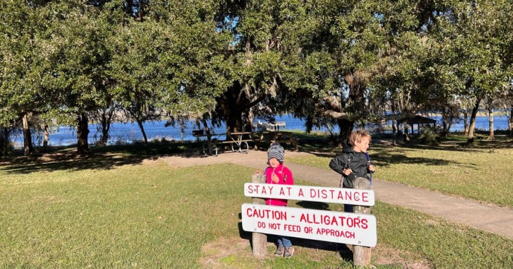 Children standing near a sign warning people to keep a safe distance from alligators